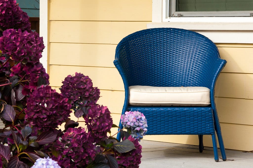 Blue wicker chair on a sunny beach house porch with hydrangeas